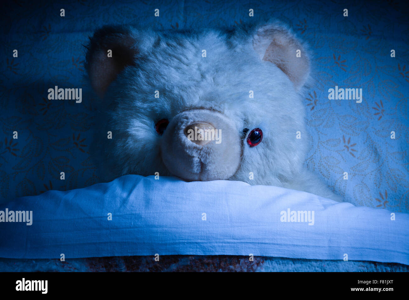 Ruined Old Teddy Bear Laying on a Bed at Night Stock Photo