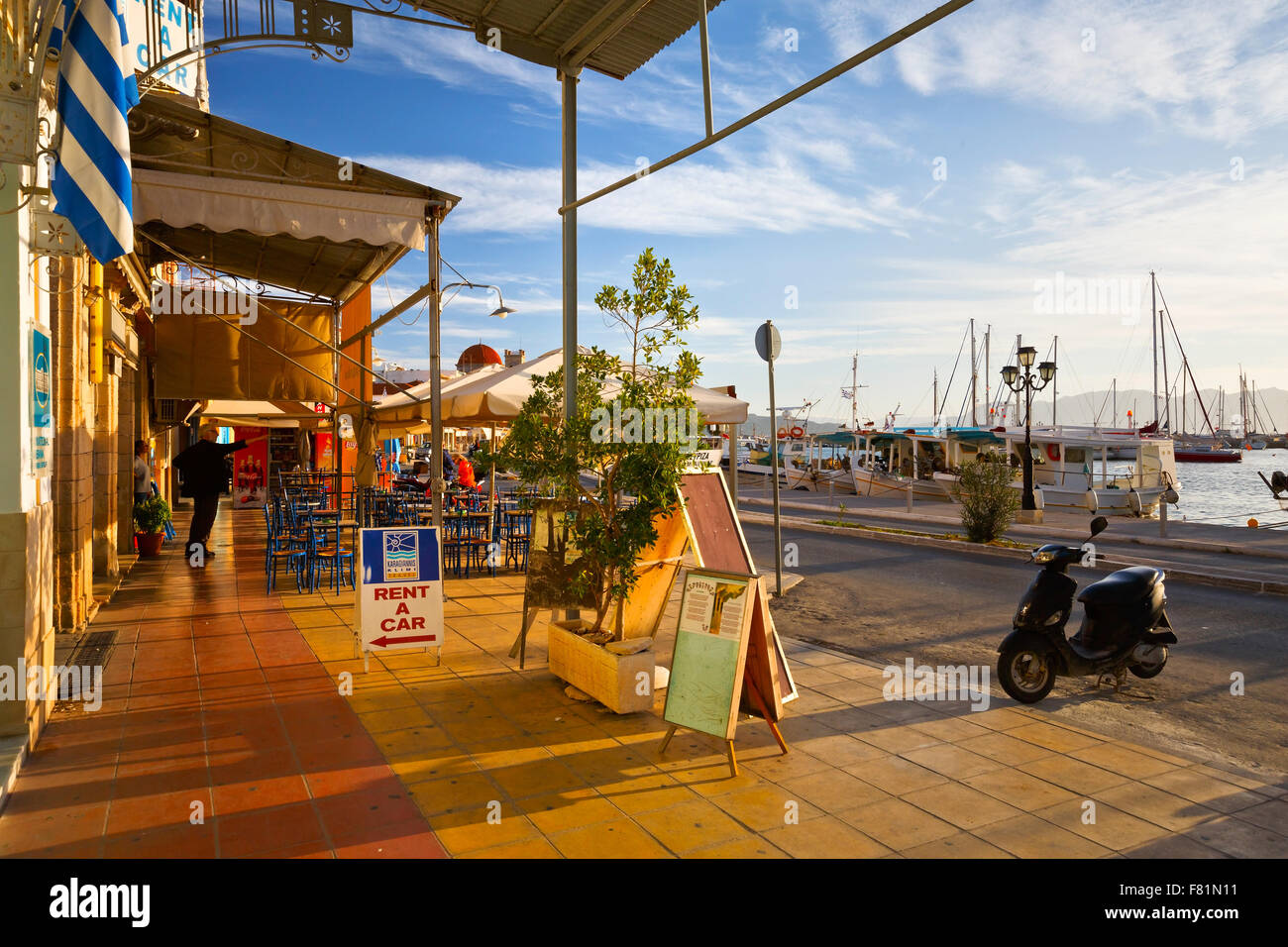 Street view of the coffee shops, bars and restaurants and the harbour of Aegina town, Greece Stock Photo