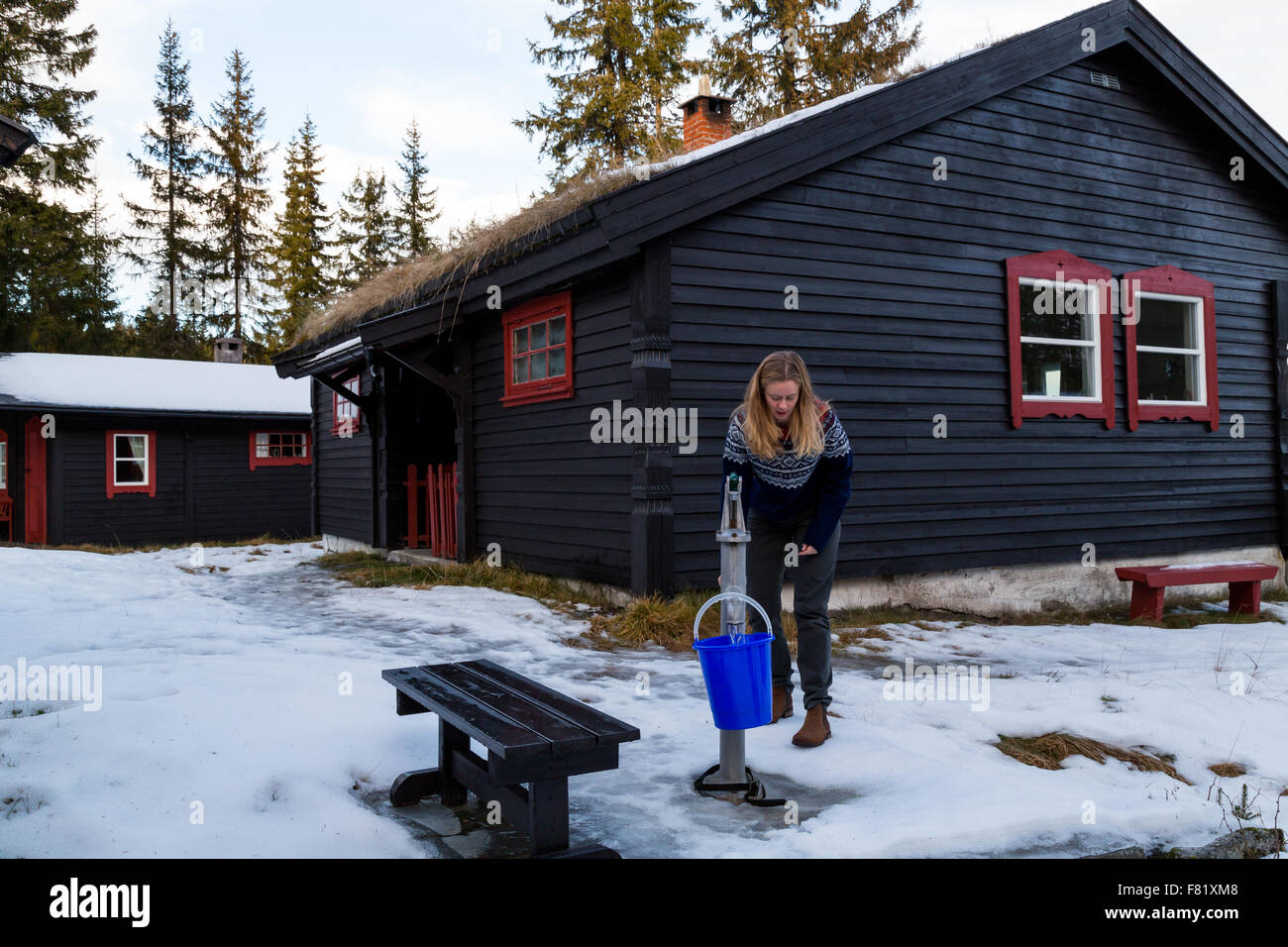 Pretty girl filling a bucket using a hand pump from a well outside a cabin in the forest North of Oslo - landscape Stock Photo