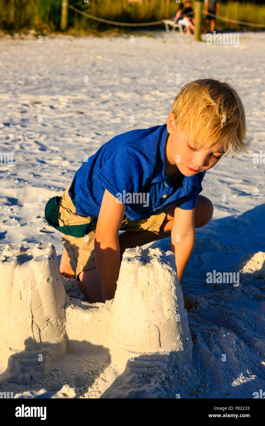 Young boy posing at sunset by the sand castle she built on Siesta Key beach in Florida Stock Photo