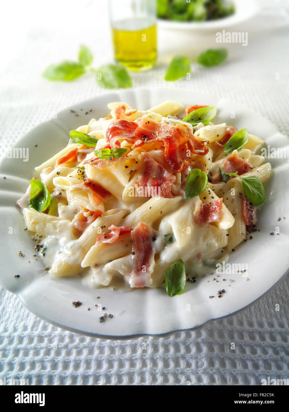 Fresh cooked pene bacon and cheese carbonara, plated and garnished with basil Stock Photo