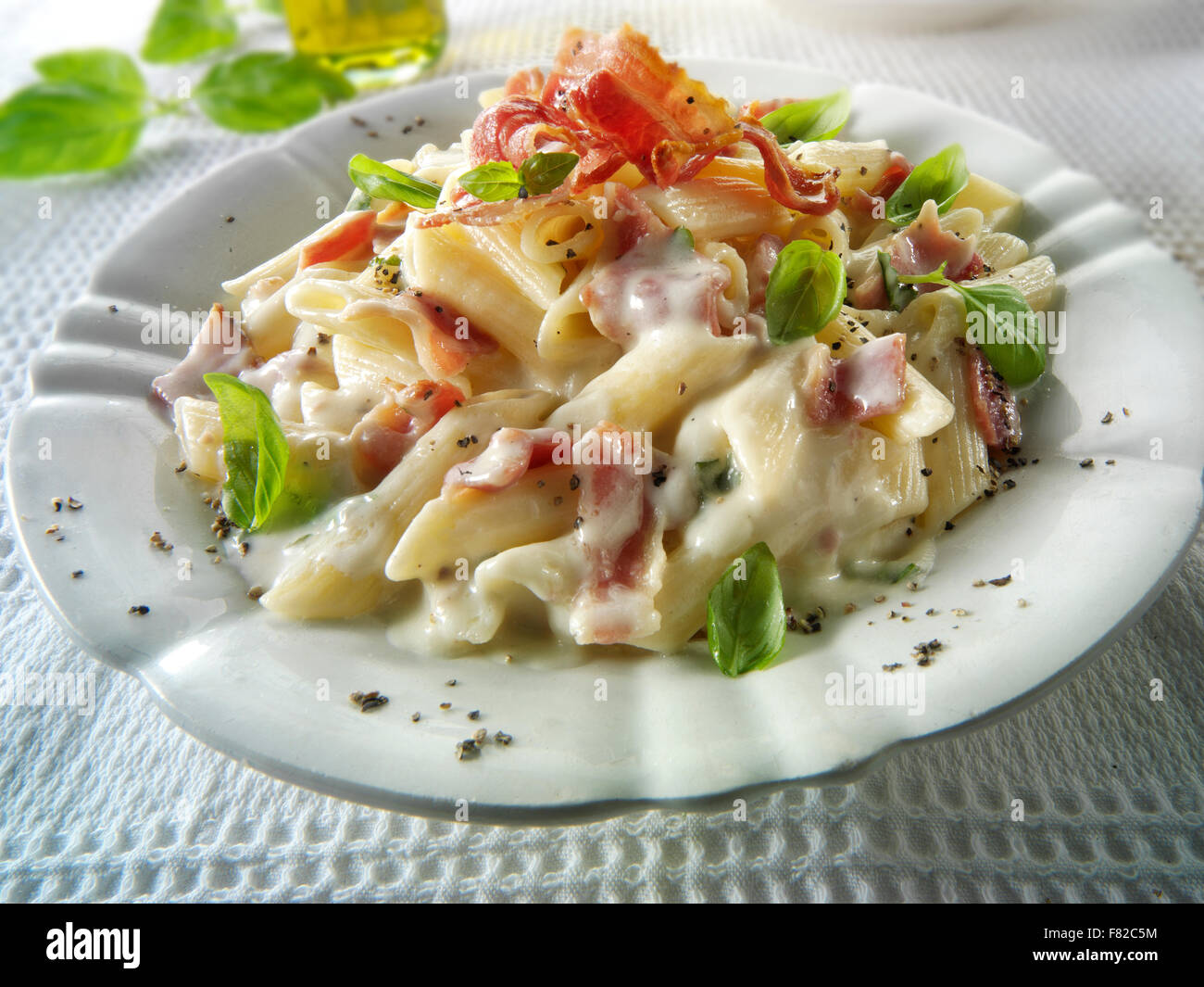 Fresh cooked pene bacon and cheese carbonara, plated and garnished with basil Stock Photo