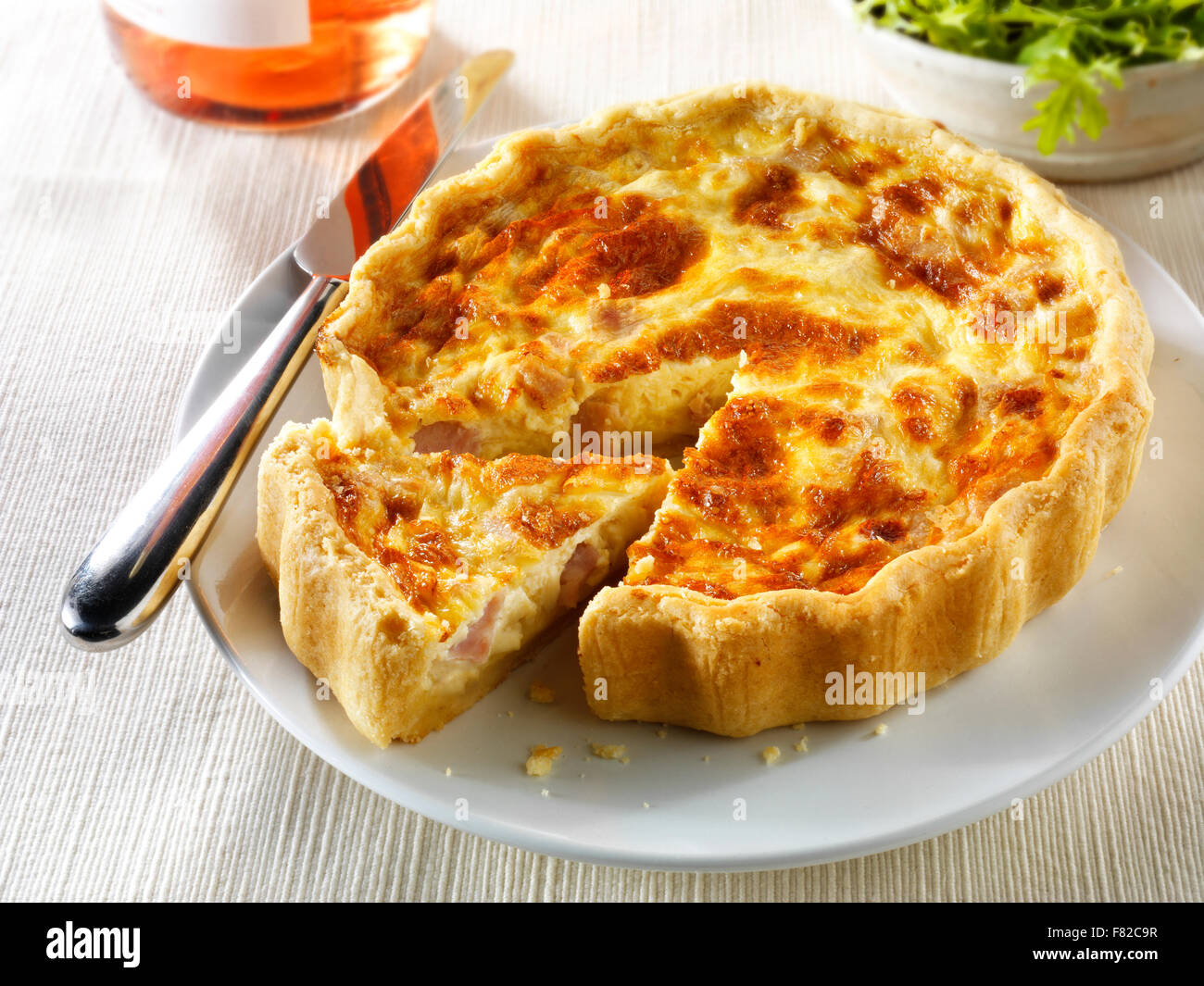 Whole quiche Loraine in a lunch time setting with a cut slice Stock Photo