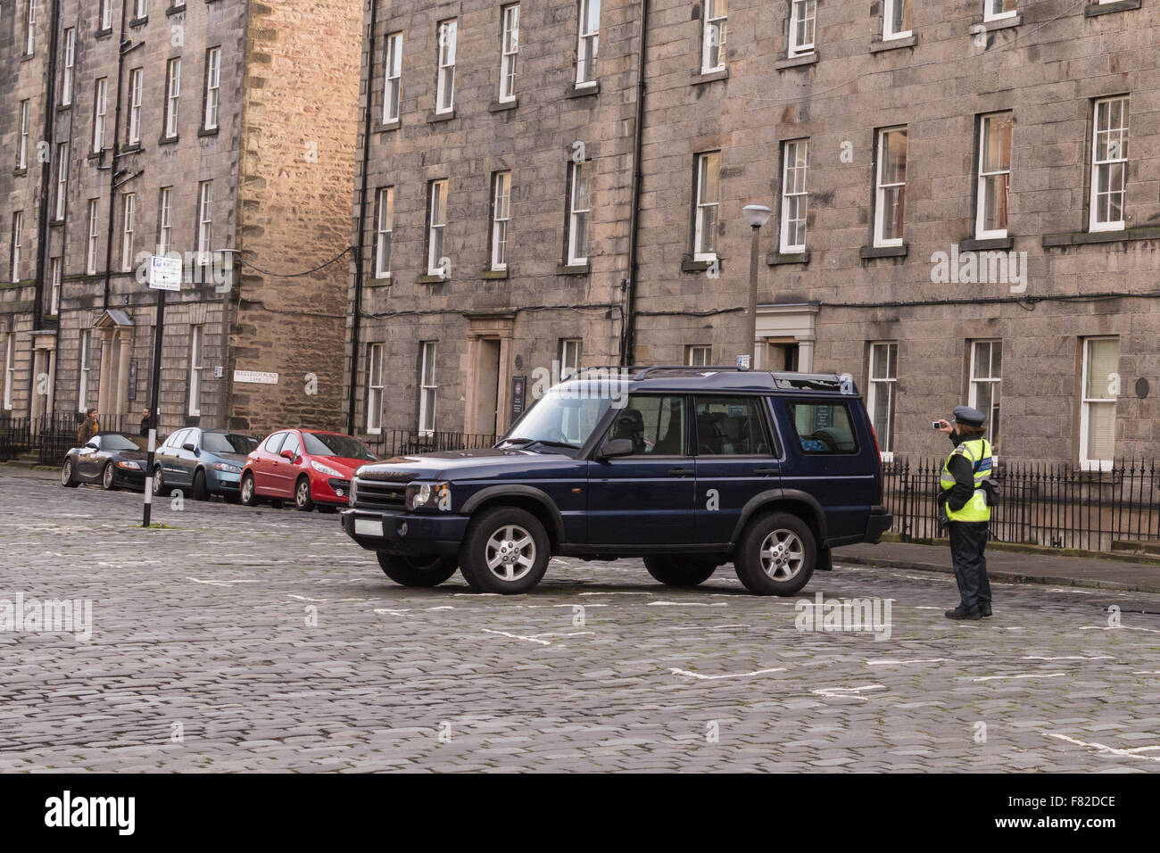 Parking Attendant (traffic wardens not longer used) photographs a land rover parked in Buccleuch Place, Edinburgh, Scotland, UK Stock Photo