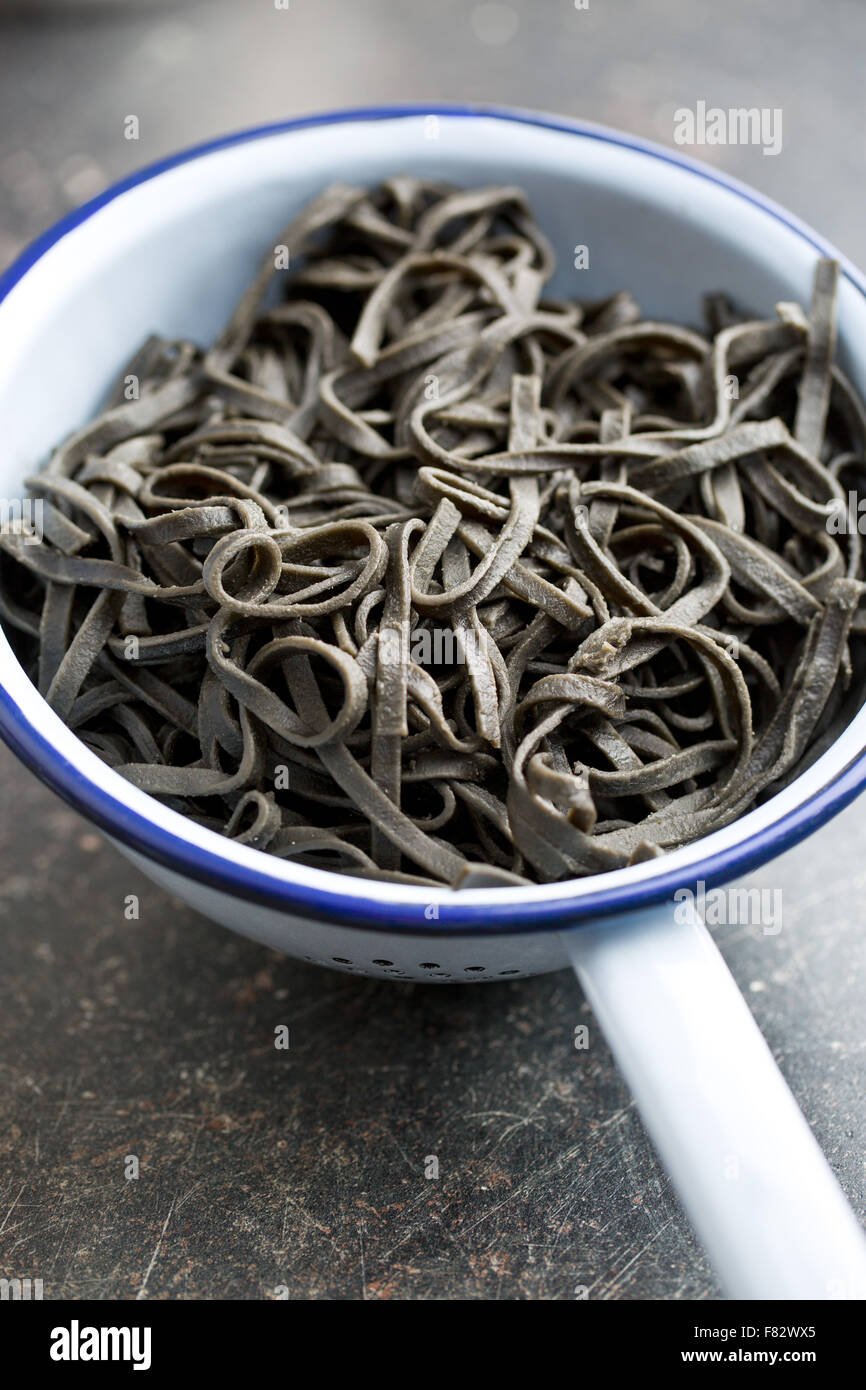 cooked black noodles with squid sepia ink in colander Stock Photo