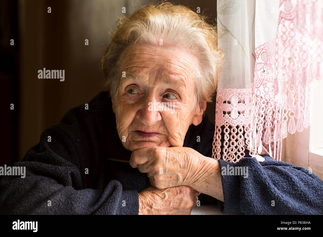 Old woman sitting near the window, a close-up portrait. Stock Photo