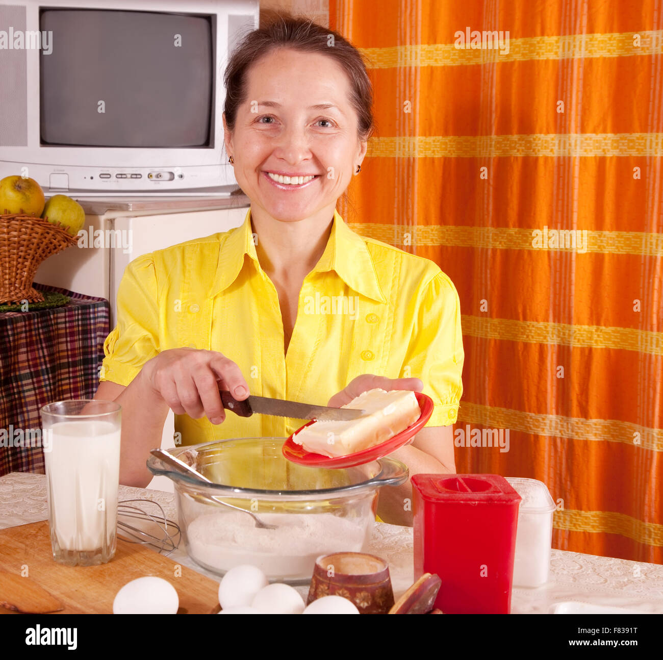 Smiling woman adds margarine into dough in kitchen Stock Photo