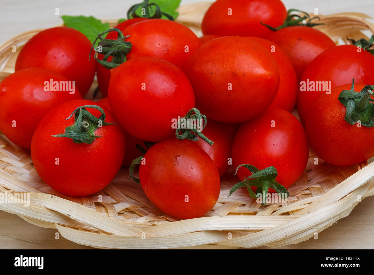 Cherry tomatoes in the basket with fresh green leaf Stock Photo - Alamy