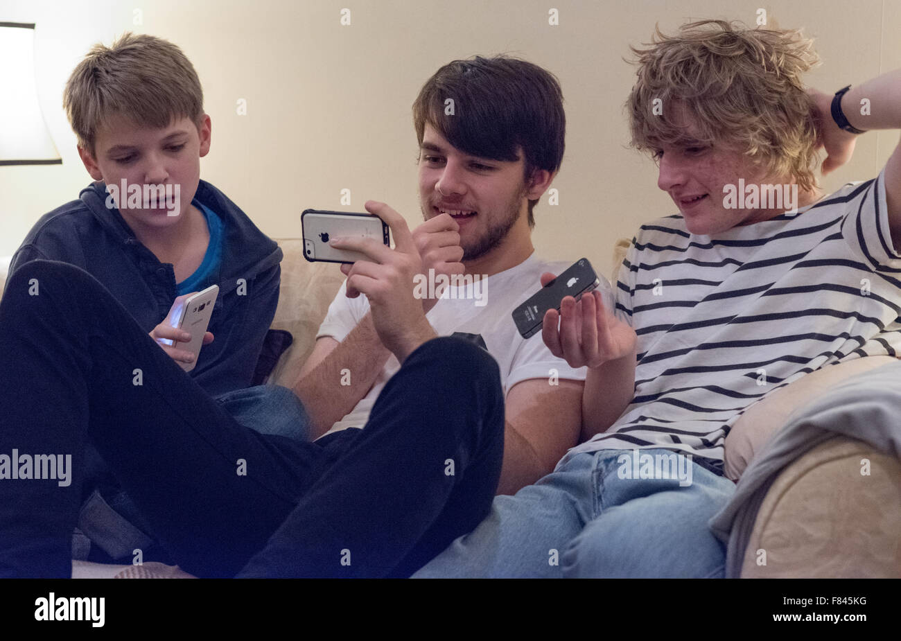 Three good-looking white happy teenage boys laughing and looking at their mobile phones playing online games, watching YouTube and on social meida Stock Photo