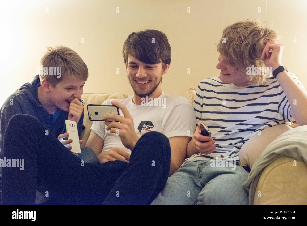 Three good-looking white happy teenage boys laughing and looking at their mobile phones playing online games, watching YouTube and on social meida Stock Photo