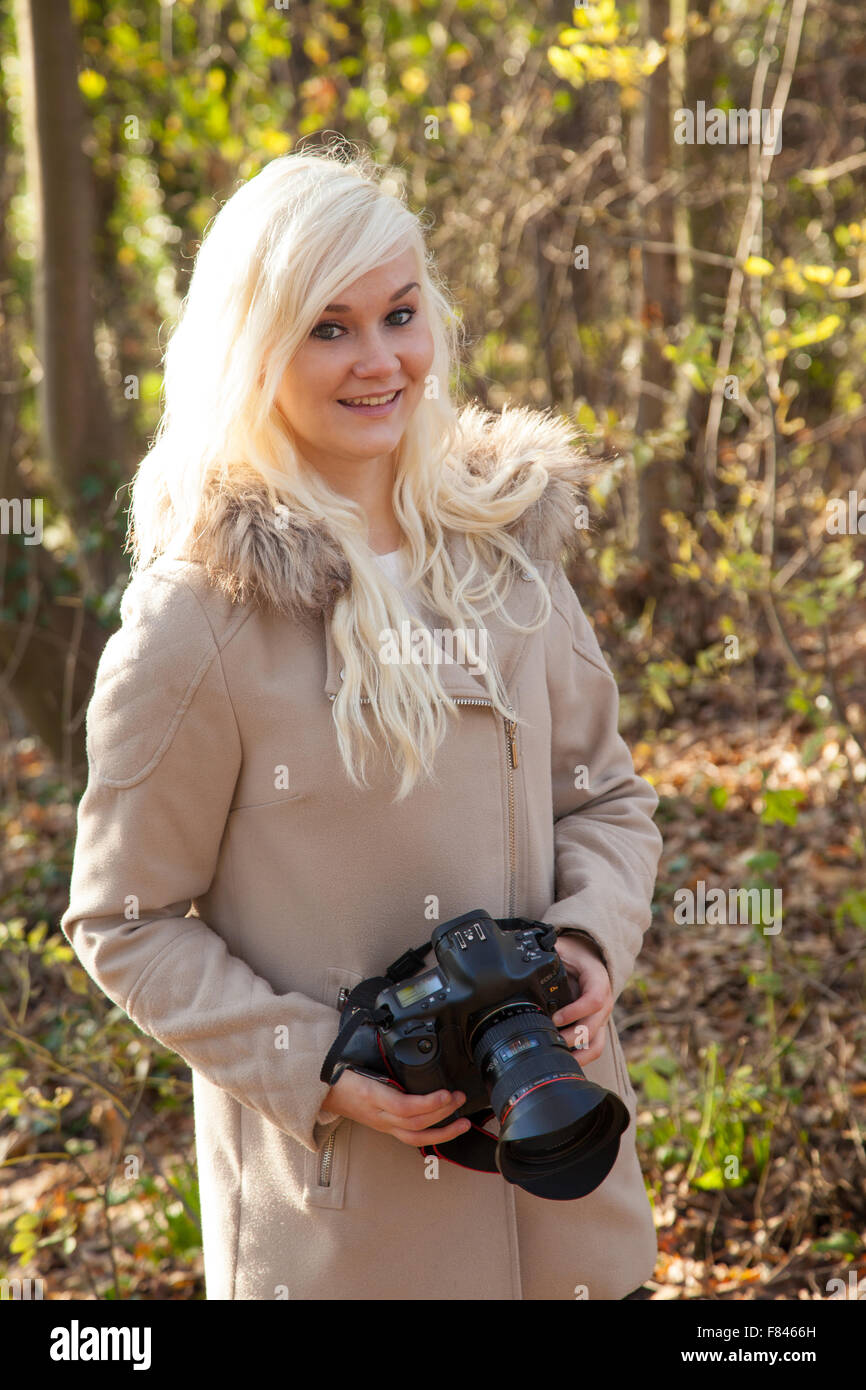 Pretty blond woman holding a DSLR camera outside. Stock Photo