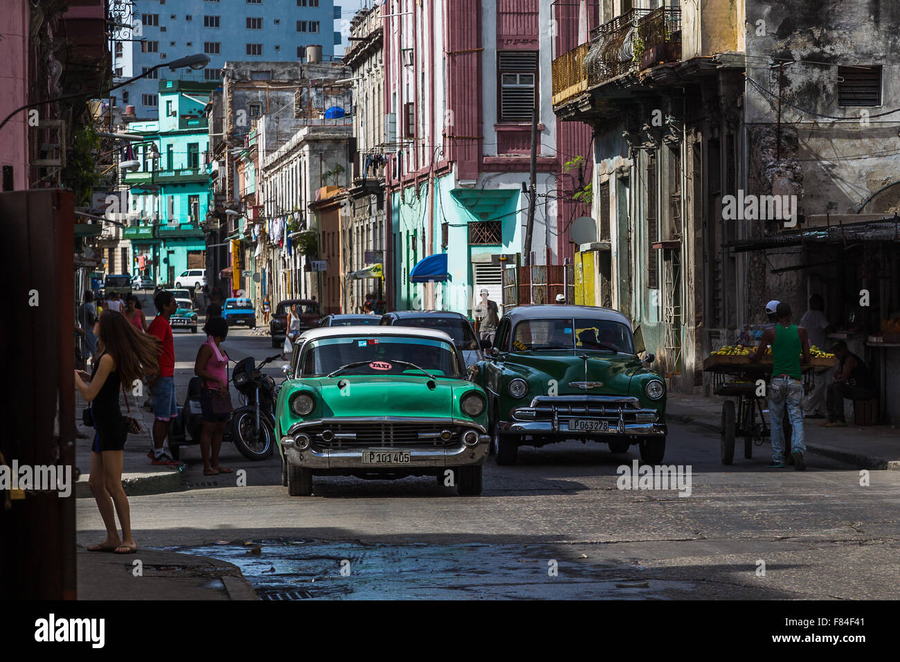 A pair of green classical cars in Centro Havana emerge from the shadows cast by the rising sun as they had towards the old town. Stock Photo