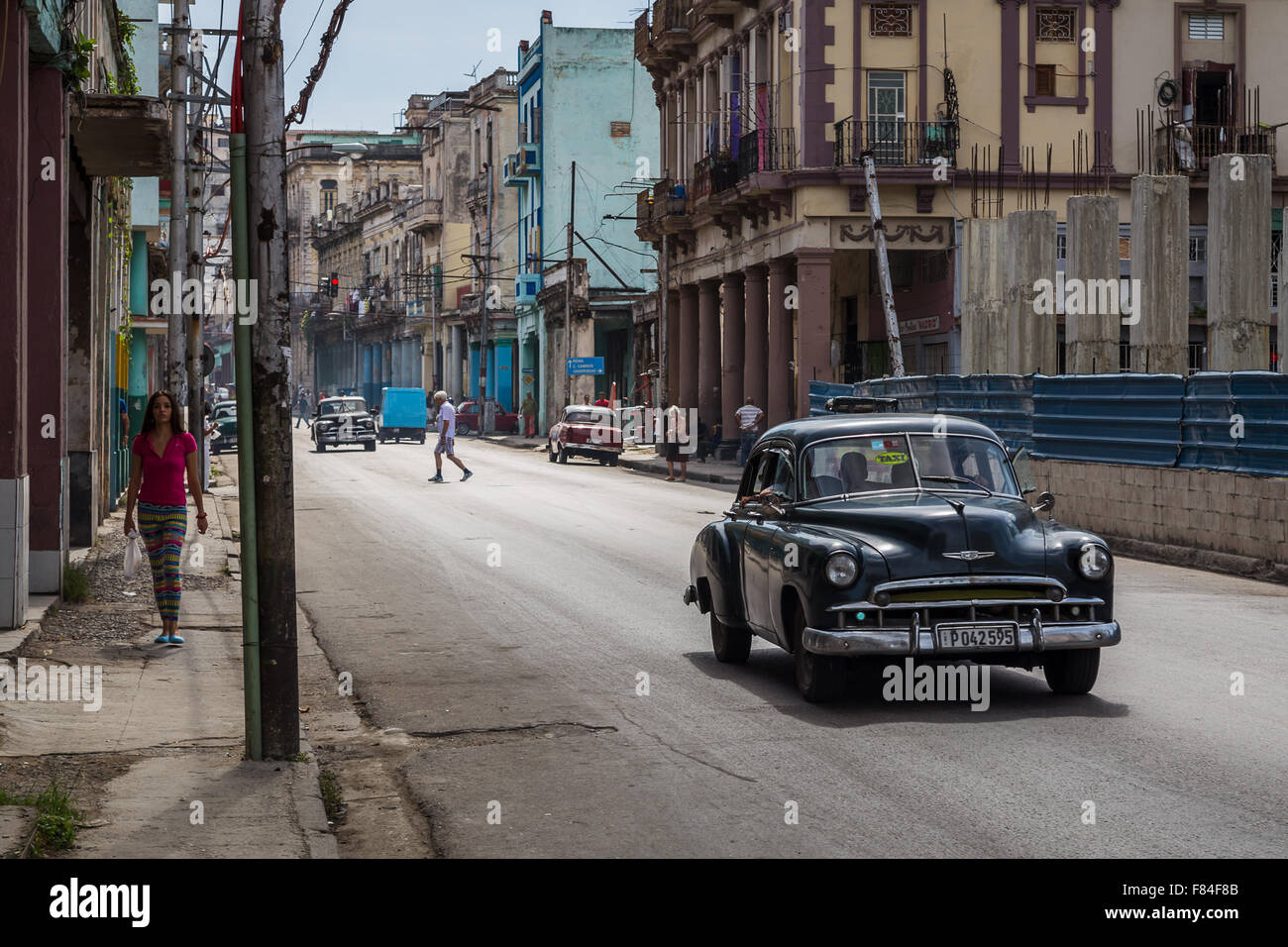 A taxi seen passing a lady wearing pink in Centro Havana one lunchtime whilst walking the streets of Havana. Stock Photo
