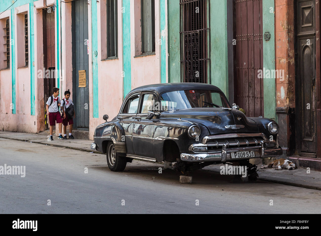 School boys walk passed a sleeping dog & an old timer on bricks on their way home in Centro Havana. Stock Photo