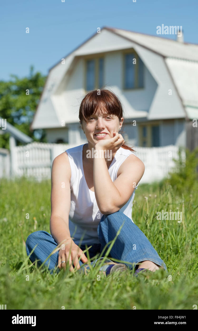 Happy young woman sitting on lawn in front of new home Stock Photo - Alamy