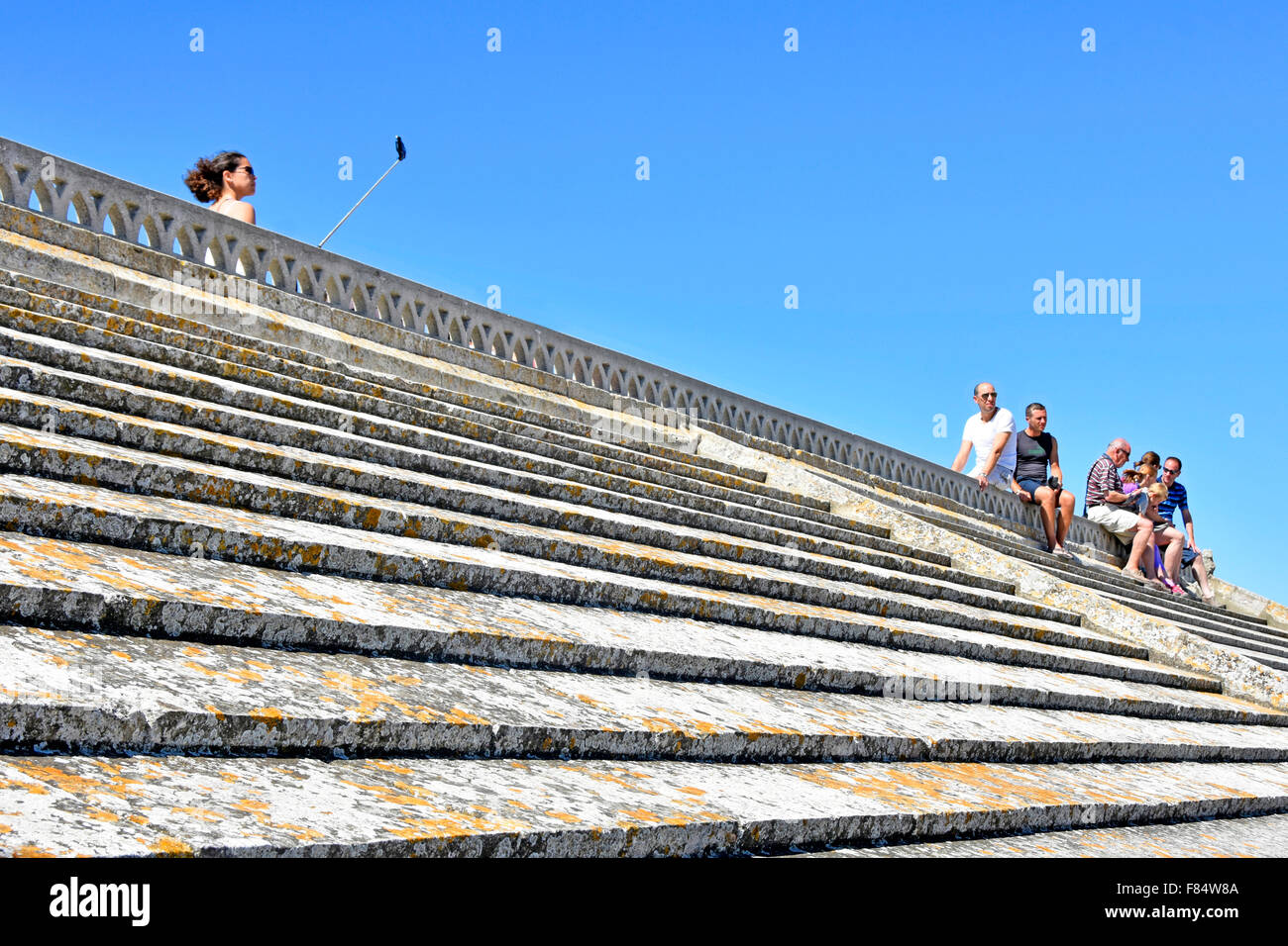 Woman taking a selfie picture & holiday tourists paying for sightseeing on roof of the church Les Saintes-Maries-de-la-Mer in Saintes Maries de la Mer Stock Photo