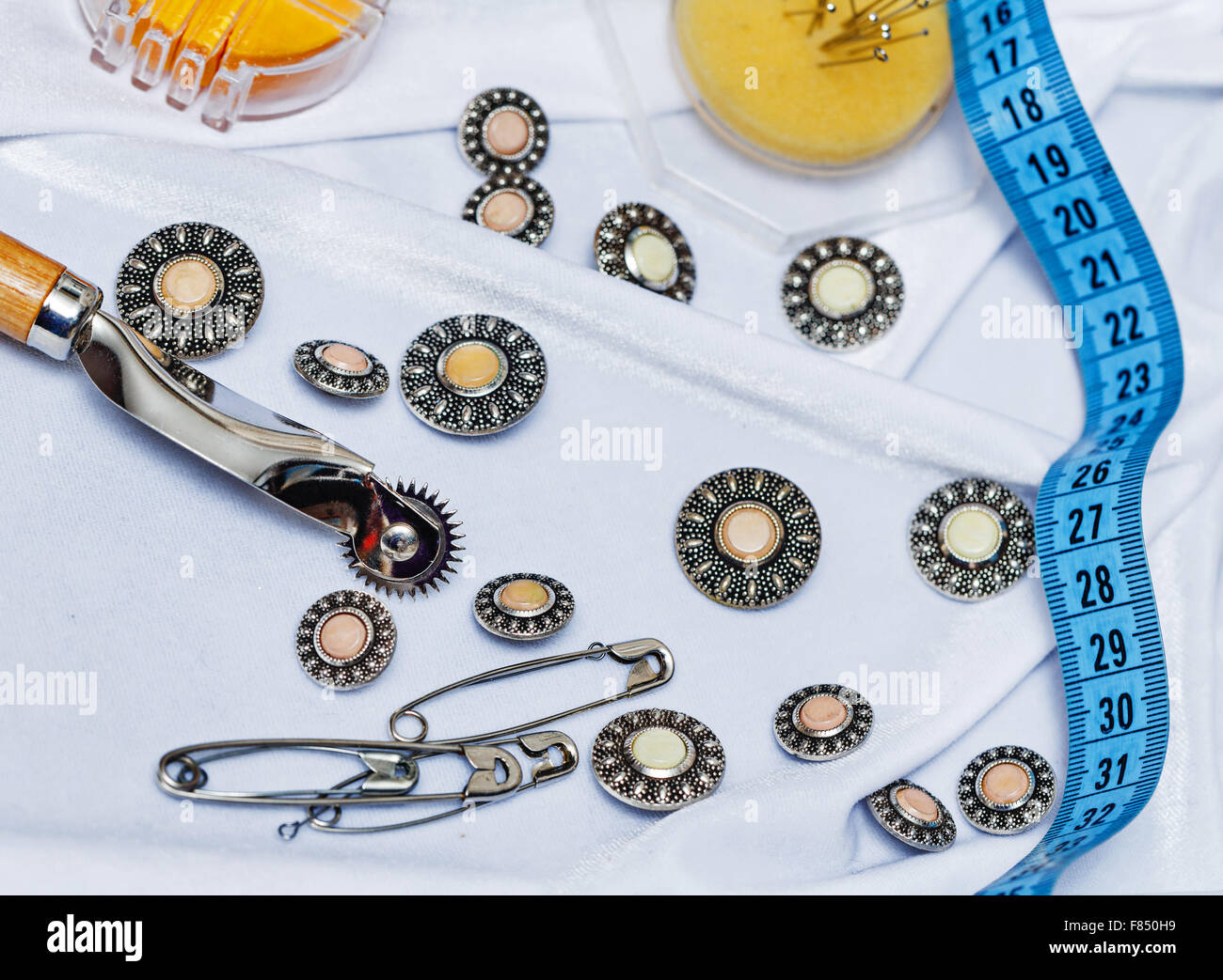 Buttons, pins, measuring tape and a needle lying on the silk cloth. The