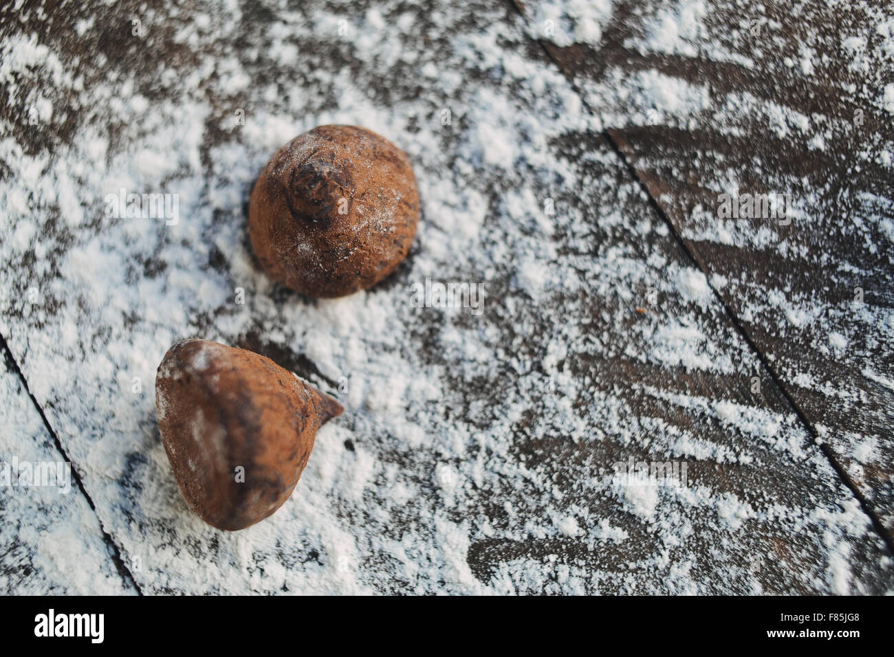 Two chocolate truffles in flour on rustic brown table Stock Photo