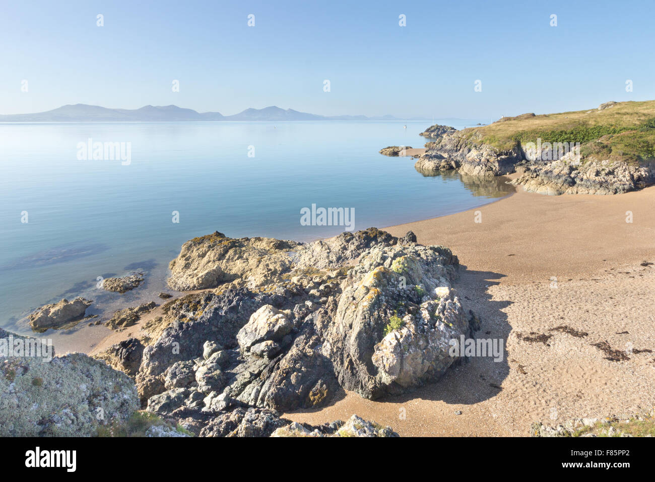 Volcanic rock and beach on Llanddwyn Island, Anglesey, Wales with the Llyn peninsula in the background Stock Photo