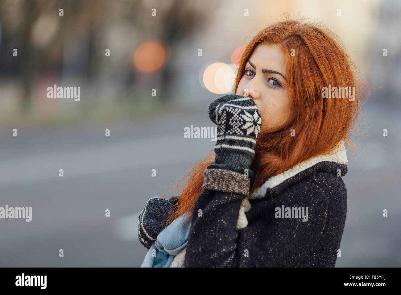 Red-haired girl standing on the street and laugh. Winter time, snow coming, sunset background Stock Photo