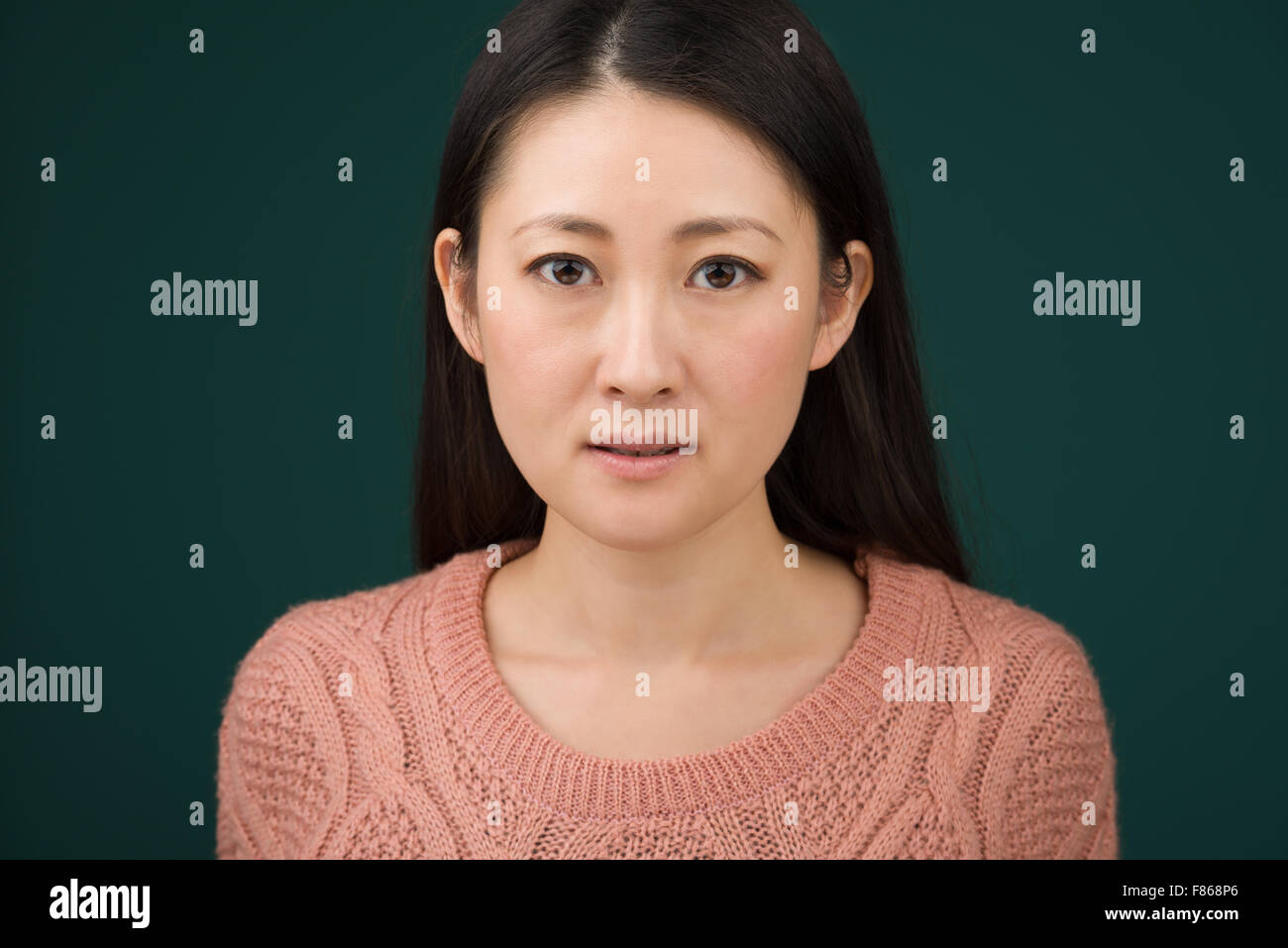 A headshot of a Japanese woman in hear early 30s on a simple green background. Stock Photo