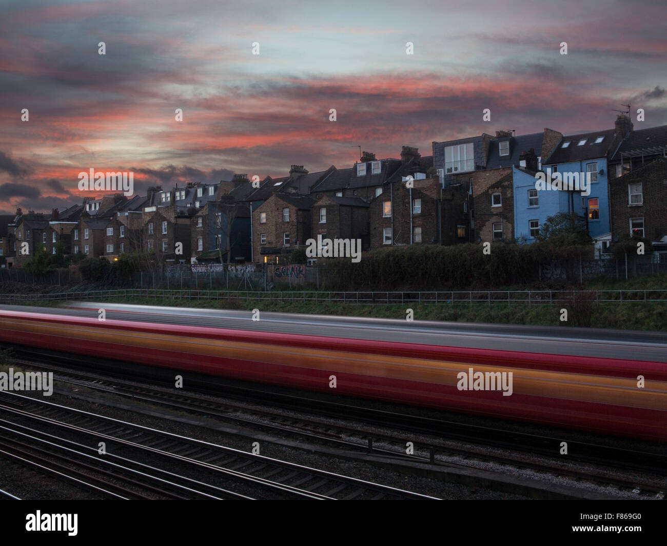 a commuter train flashes by under some terraced houses with a lovely F869G0