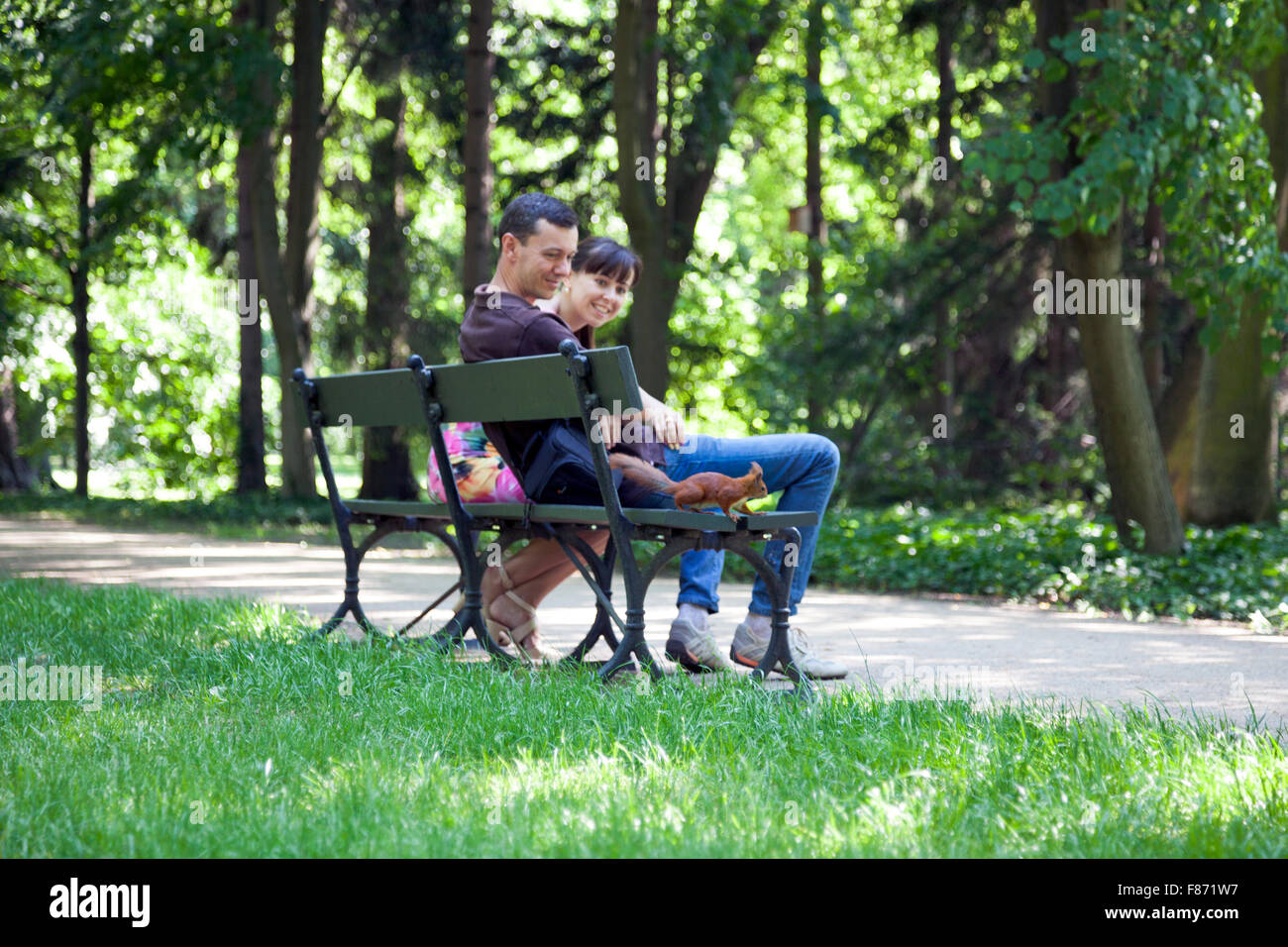 Smiling couple sitting on a park bench looks and squirrel (Lazienki Park, Warsaw, Poland) Stock Photo