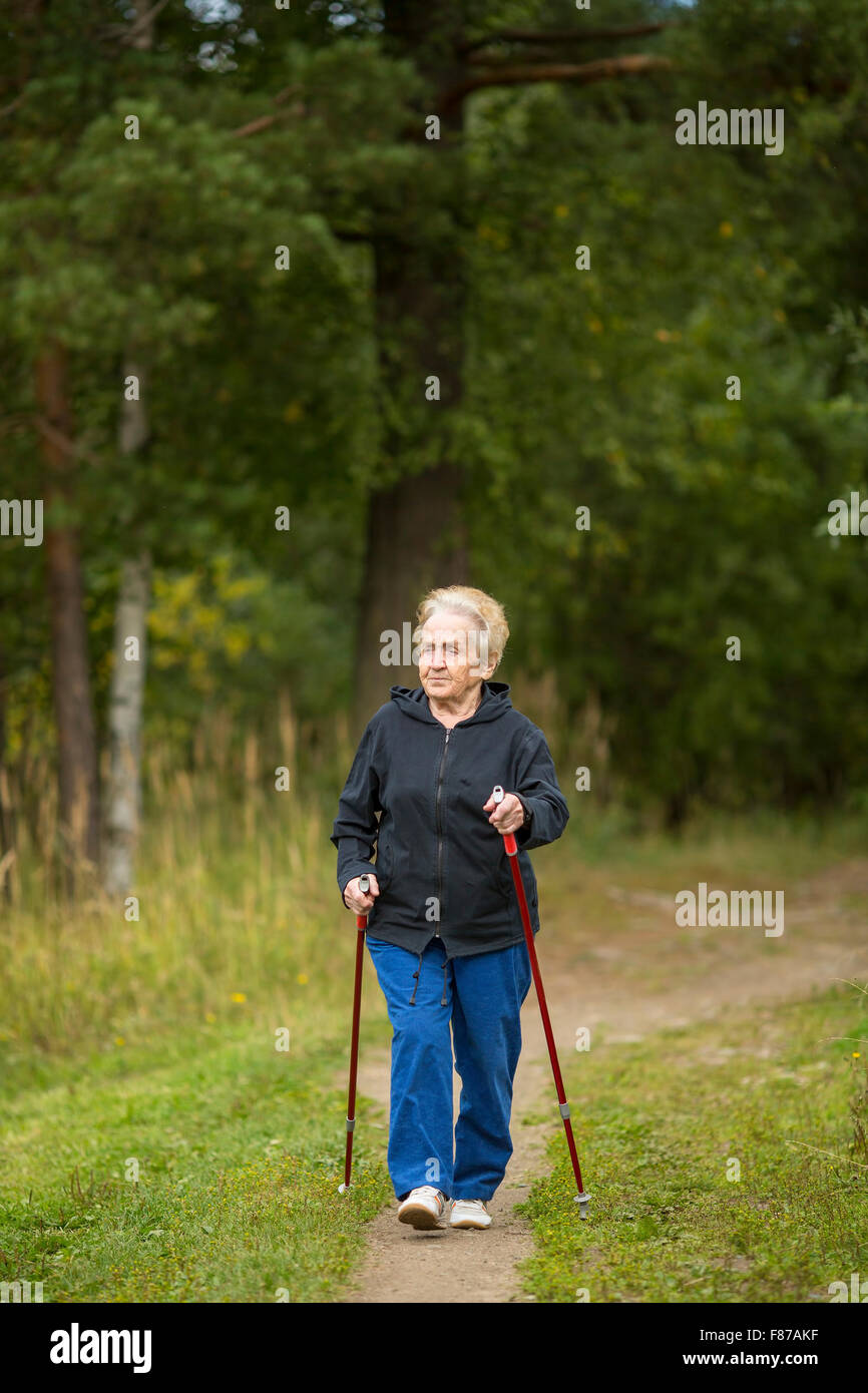 Mature woman engaged in Nordic walking in the green array. Stock Photo