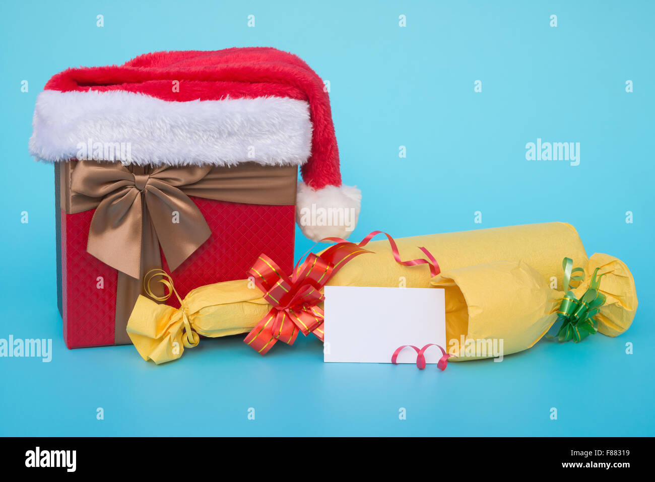 present box covered by santa claus hat and wrapped wine with blank card for text on blue background Stock Photo