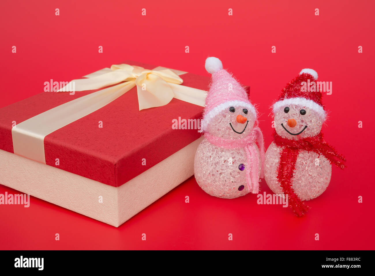 two smiling toy christmas snowman and a present box on red background Stock Photo