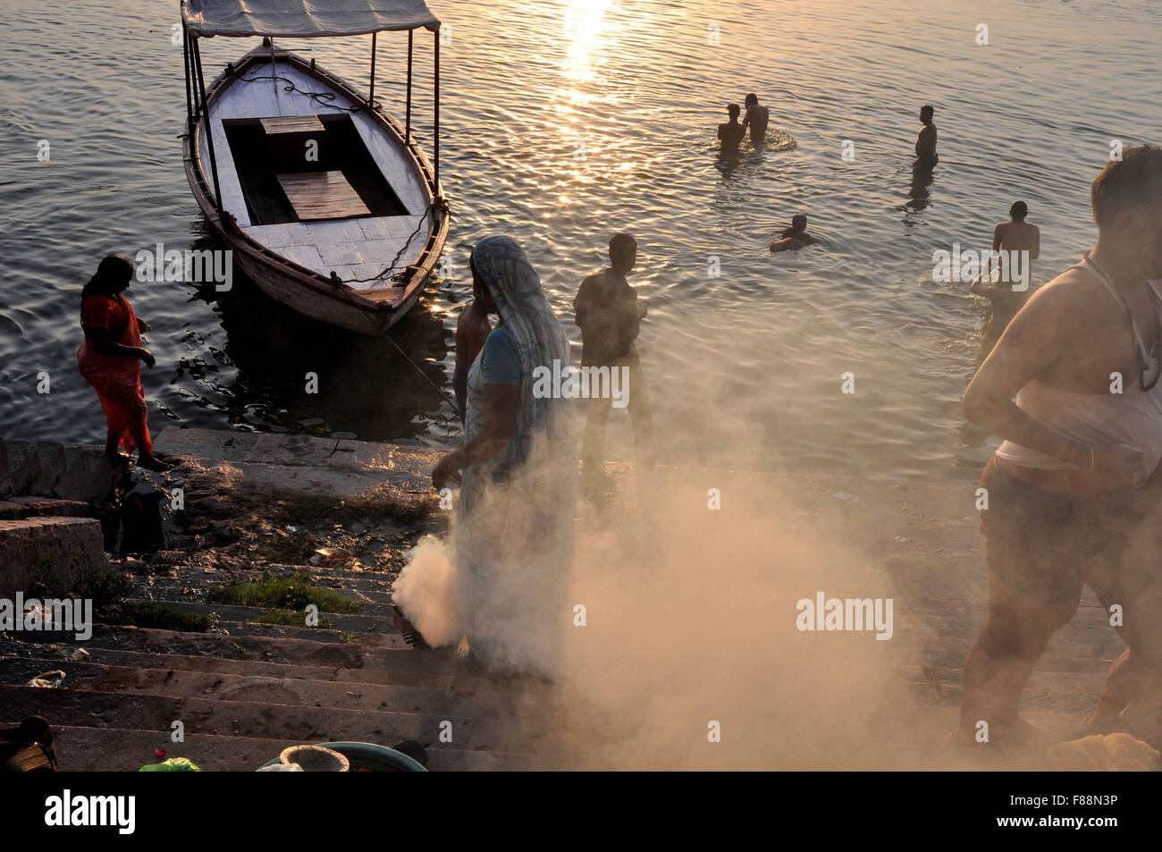Devotees taking bath and a women burning some waste material at the bank of Holy River Ganges in Varanasi, Uttar Pradesh, India. Stock Photo