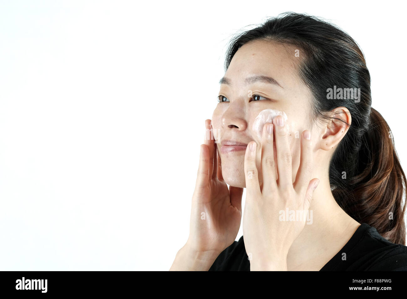Cute asian girl applying cream lotion on face, isolated on white background Stock Photo