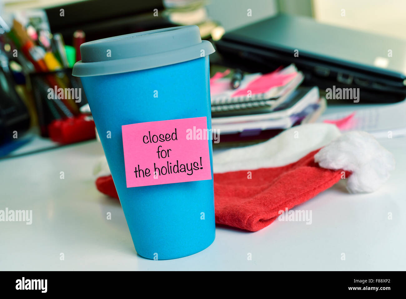 a blue mug with a pink sticky note with the text text closed for the holidays on an office desk Stock Photo