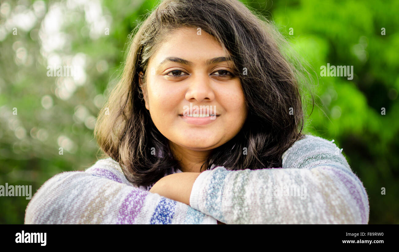 Close-up portrait of a fair chubby Indian teenage girl folded hands looking at camera over nature background. Stock Photo
