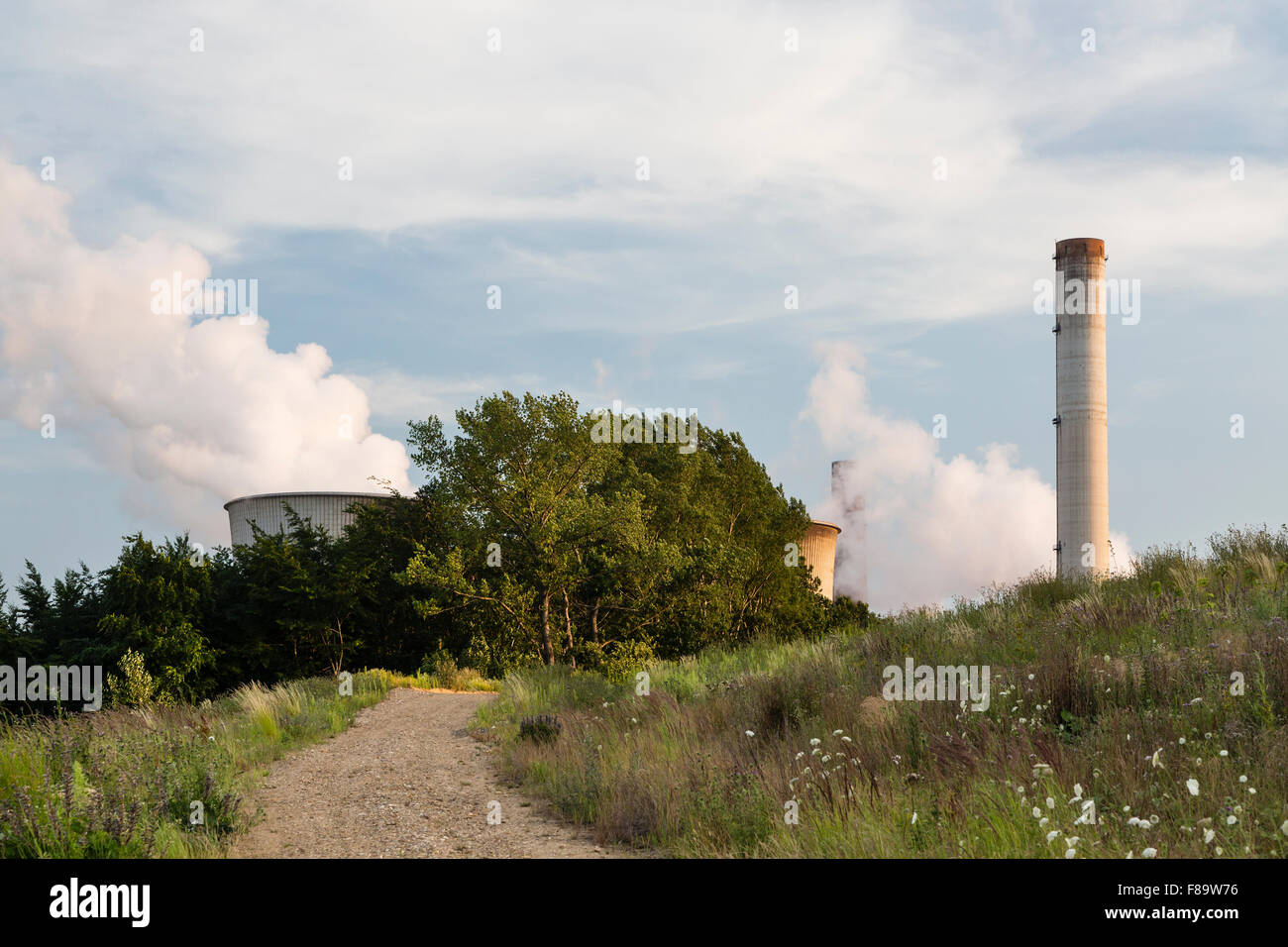 A large coal-fired power plant behind a hill with a dirt road leading towards it. Stock Photo