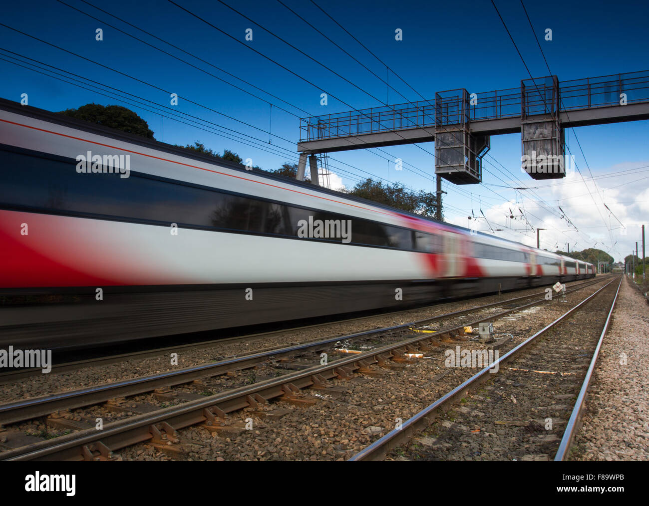A blurred high speed passenger express train traveling along railway tracks with electrified wires overhead. Stock Photo