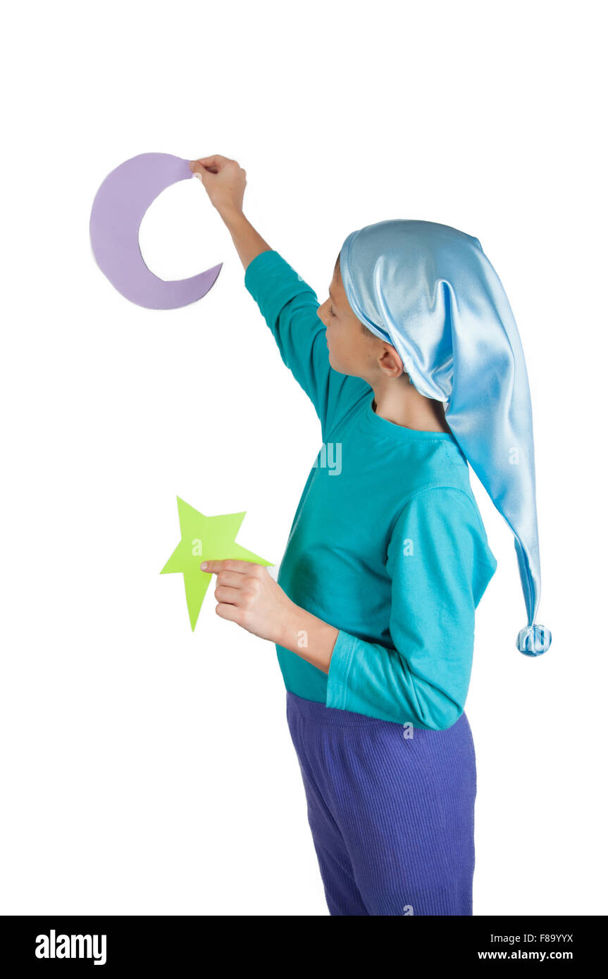 Cute boy in blue pajamas and sleeping hat holding paper moon and stars