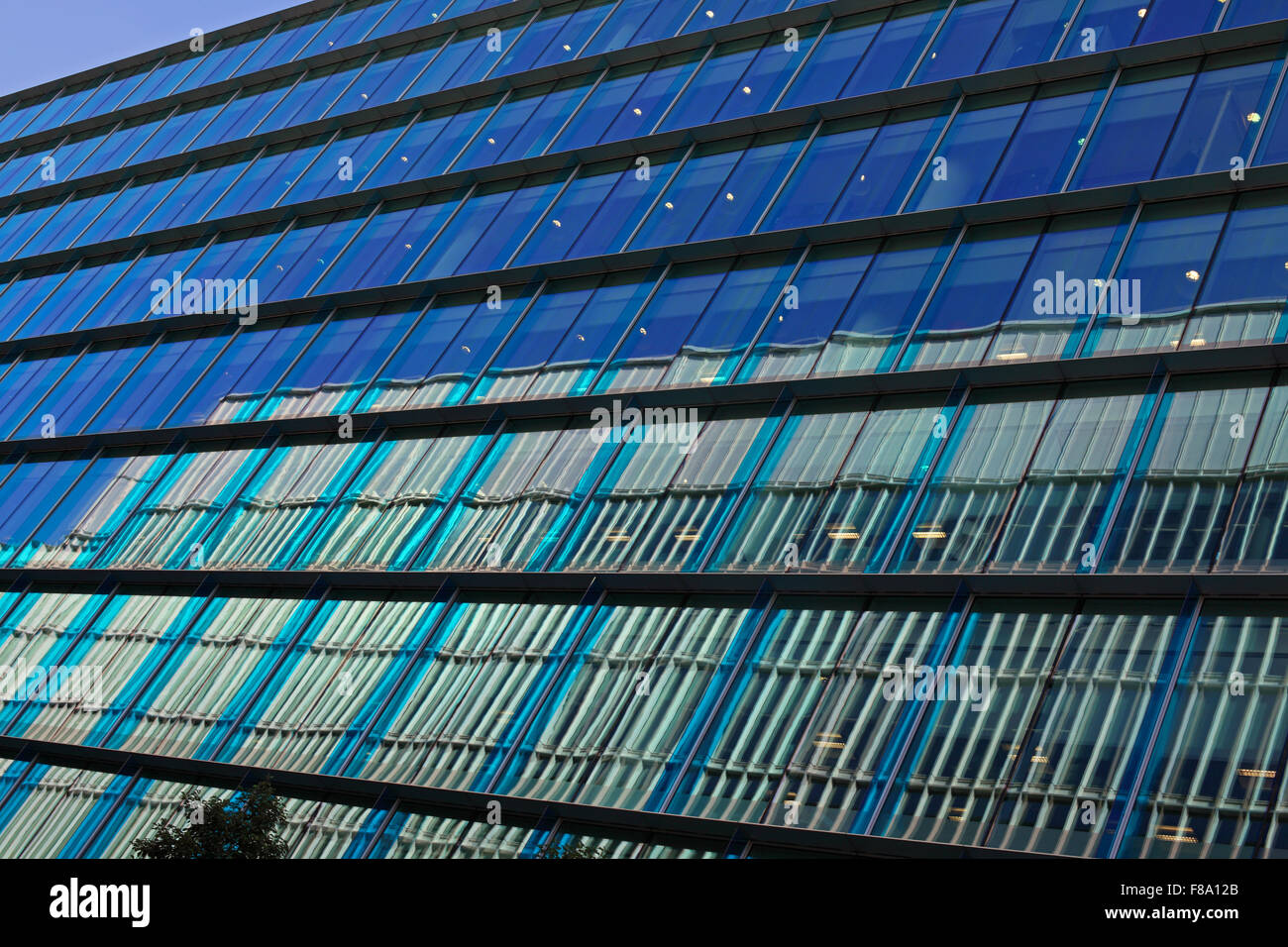 A side view of an office complex with shaded blue windows and the reflection of the opposite building in the lower windows. Stock Photo