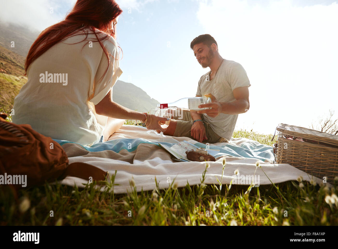 Young man pouring wine in glasses while sitting with his girlfriend. Young couple drinking wine and enjoying a picnic outdoors. Stock Photo