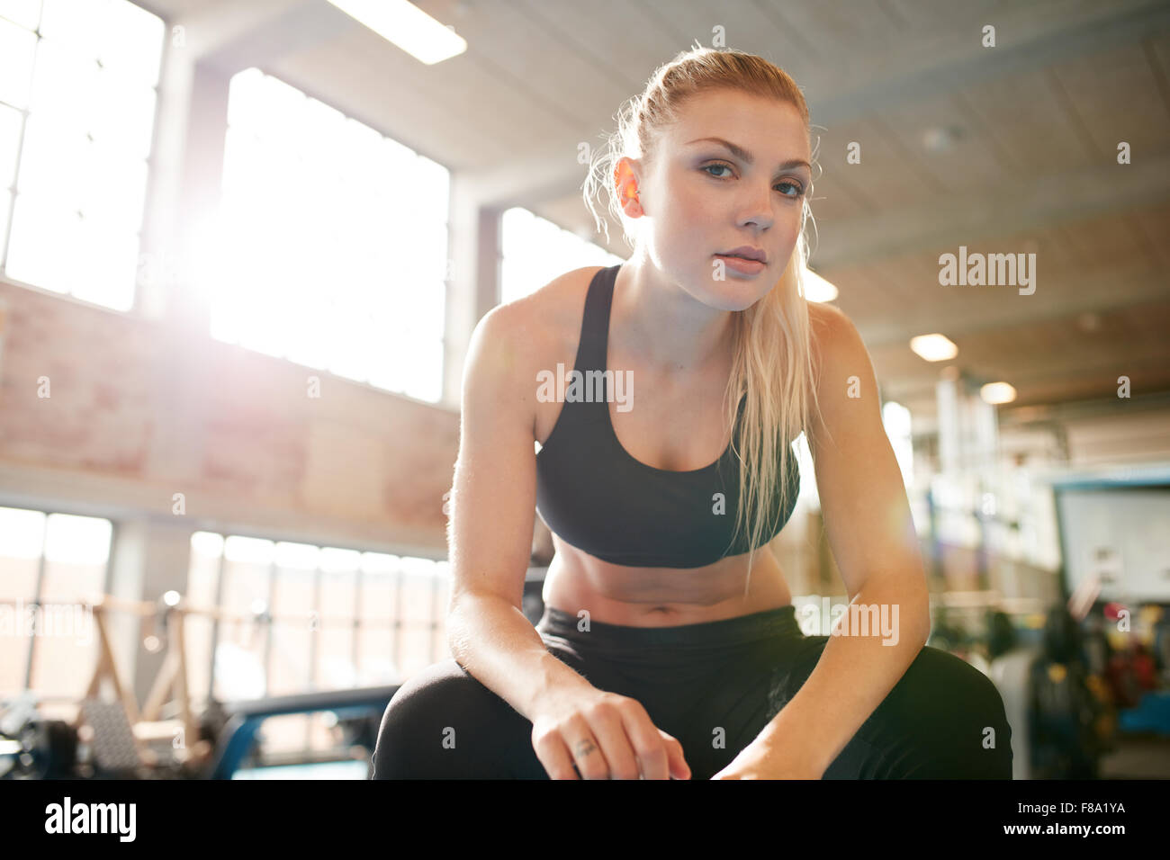 Portrait of attractive young woman sitting relaxed after her workout at gym. Fitness female taking break after exercising in hea Stock Photo