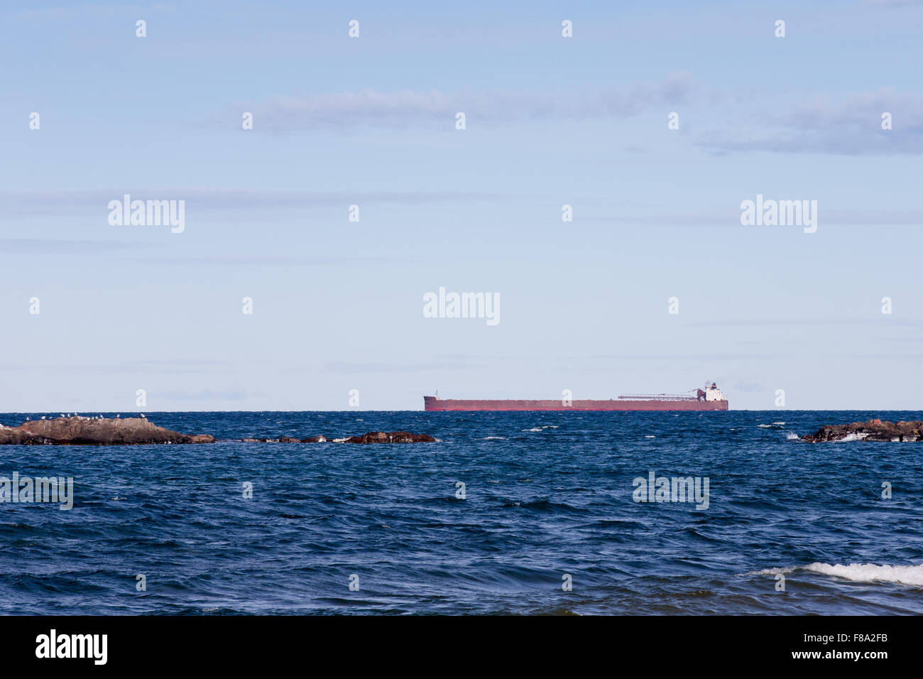 Great Lakes ore boat passing behind rocky outcroppings on Lake Superior.  Horizon is at the one-third line to allow for copy. Stock Photo