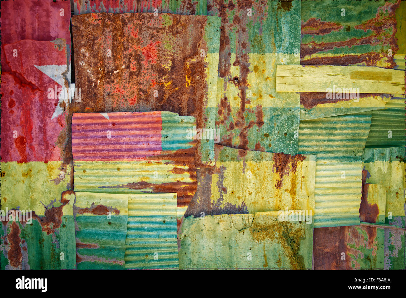 An abstract background image of the flag of Togo painted on to rusty corrugated iron sheets overlapping to form a wall or fence. Stock Photo