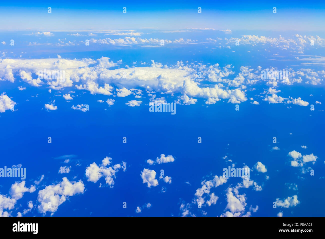View on blue sky above white clouds from the window of aircraft with skyline, horizon over ocean Stock Photo