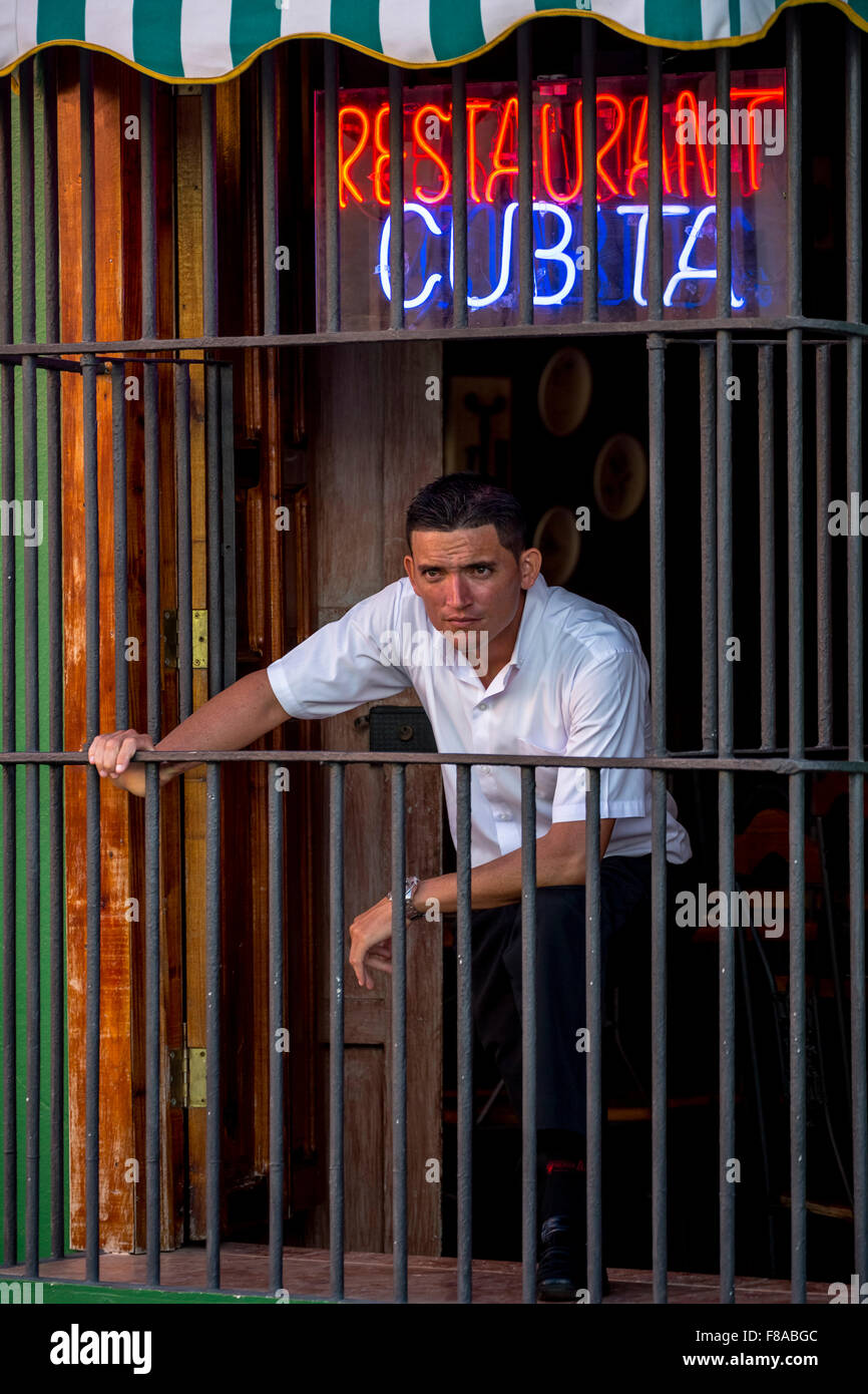 Waiter waits for clients behind the window bars of the restaurant Cubita, Trinidad, Cuba, Sancti Spíritus, Caribbean Stock Photo