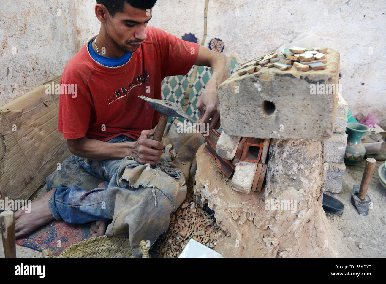 A Moroccan craftsman chiseling glazed terra cotta pieces for Zellige tilework. Stock Photo