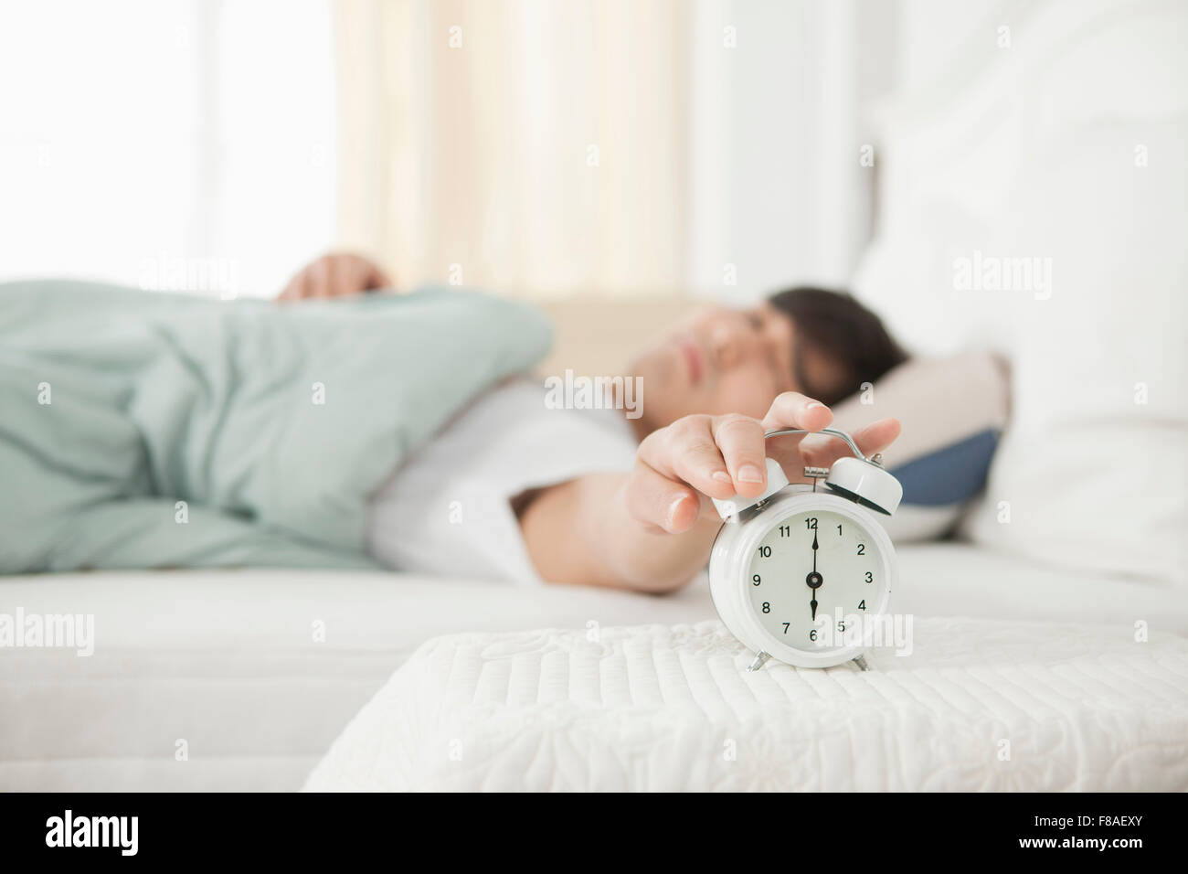 Man lying in bed and touching an alarm clock next to it Stock Photo