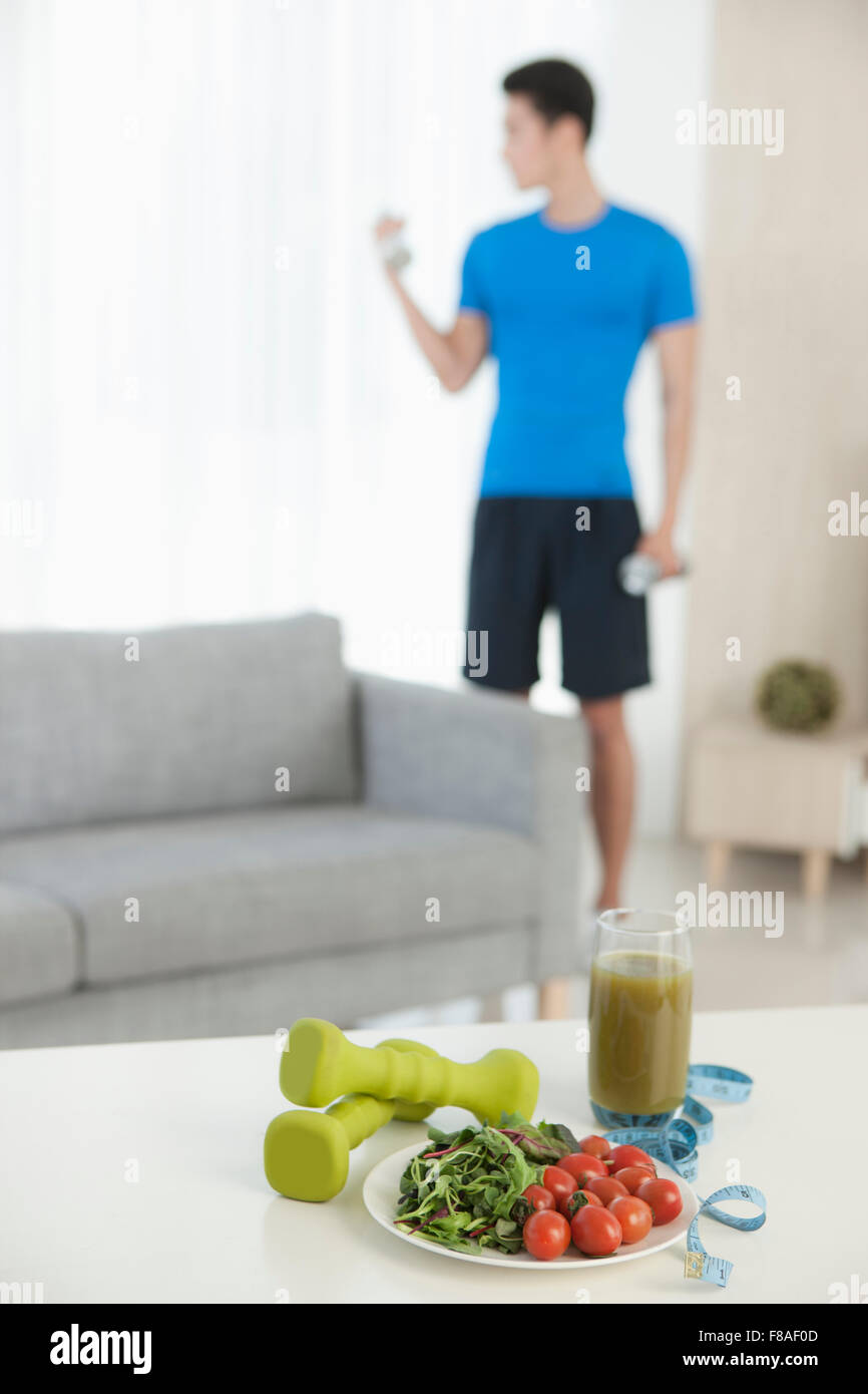 Out-focused picture of dumbbells healthy food on a table with the background of an exercising man Stock Photo