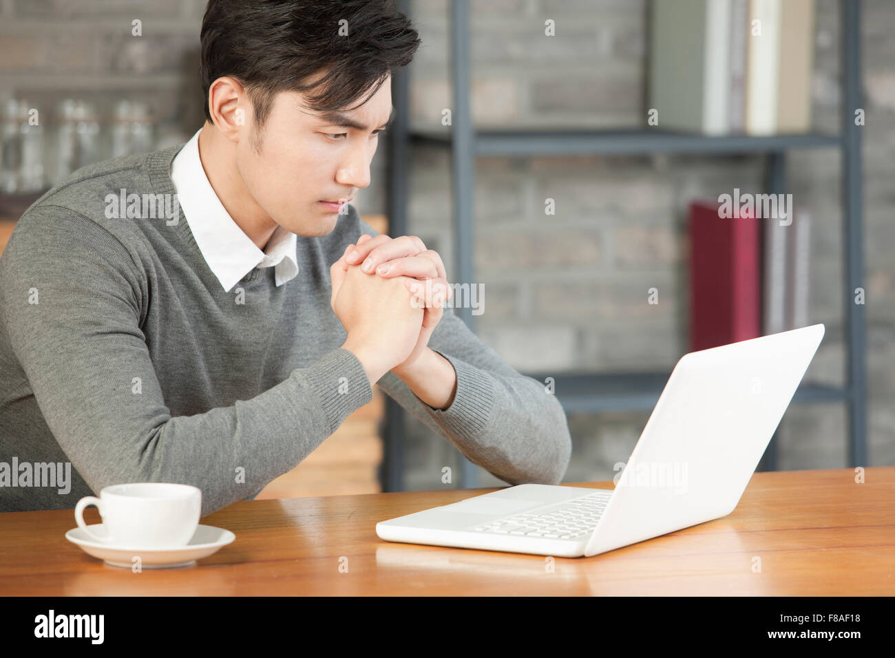 Man with hands clasped sitting at table and looking at laptop Stock Photo