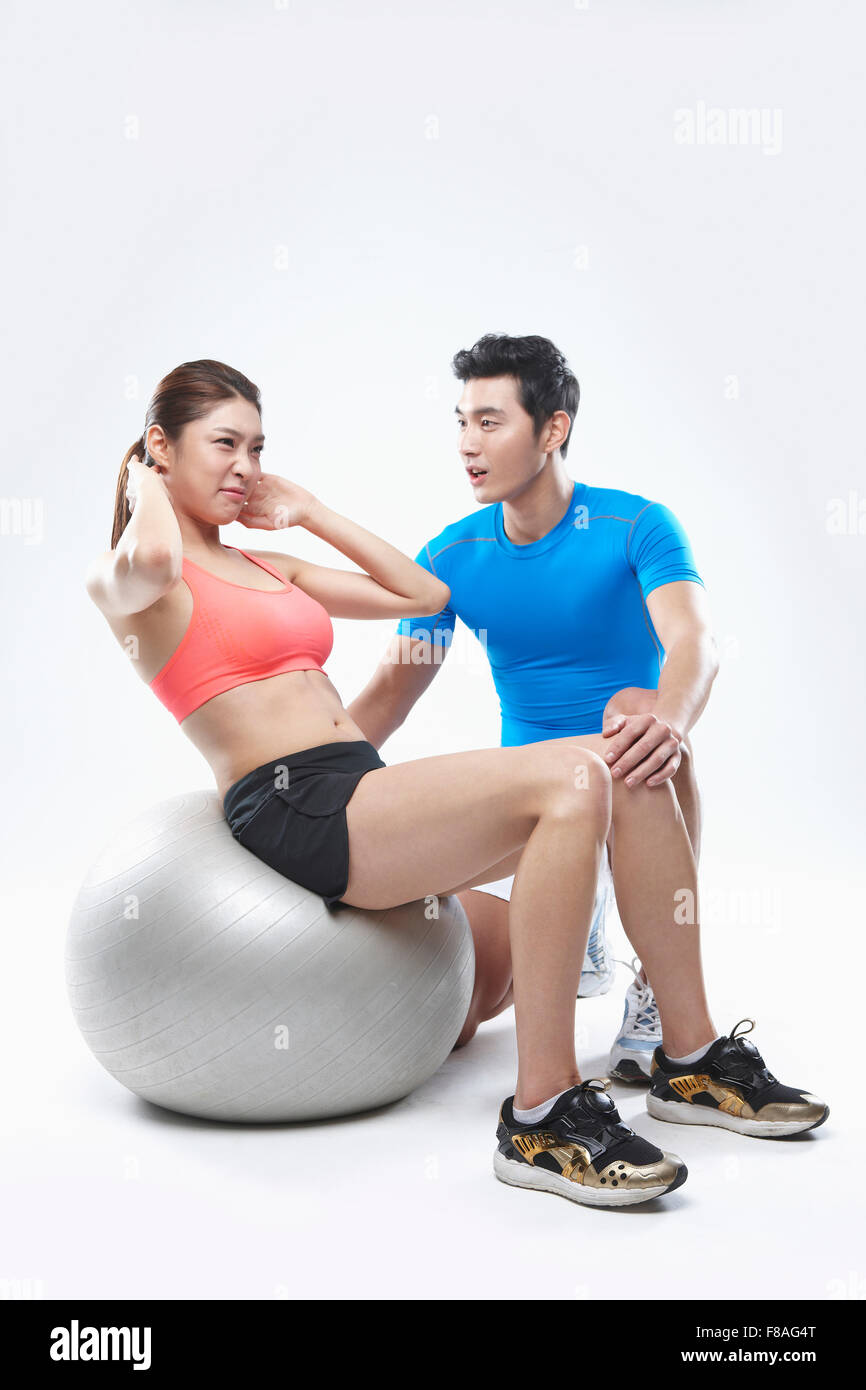 Woman doing sit-ups on gym ball and Man coaching next to her Stock Photo