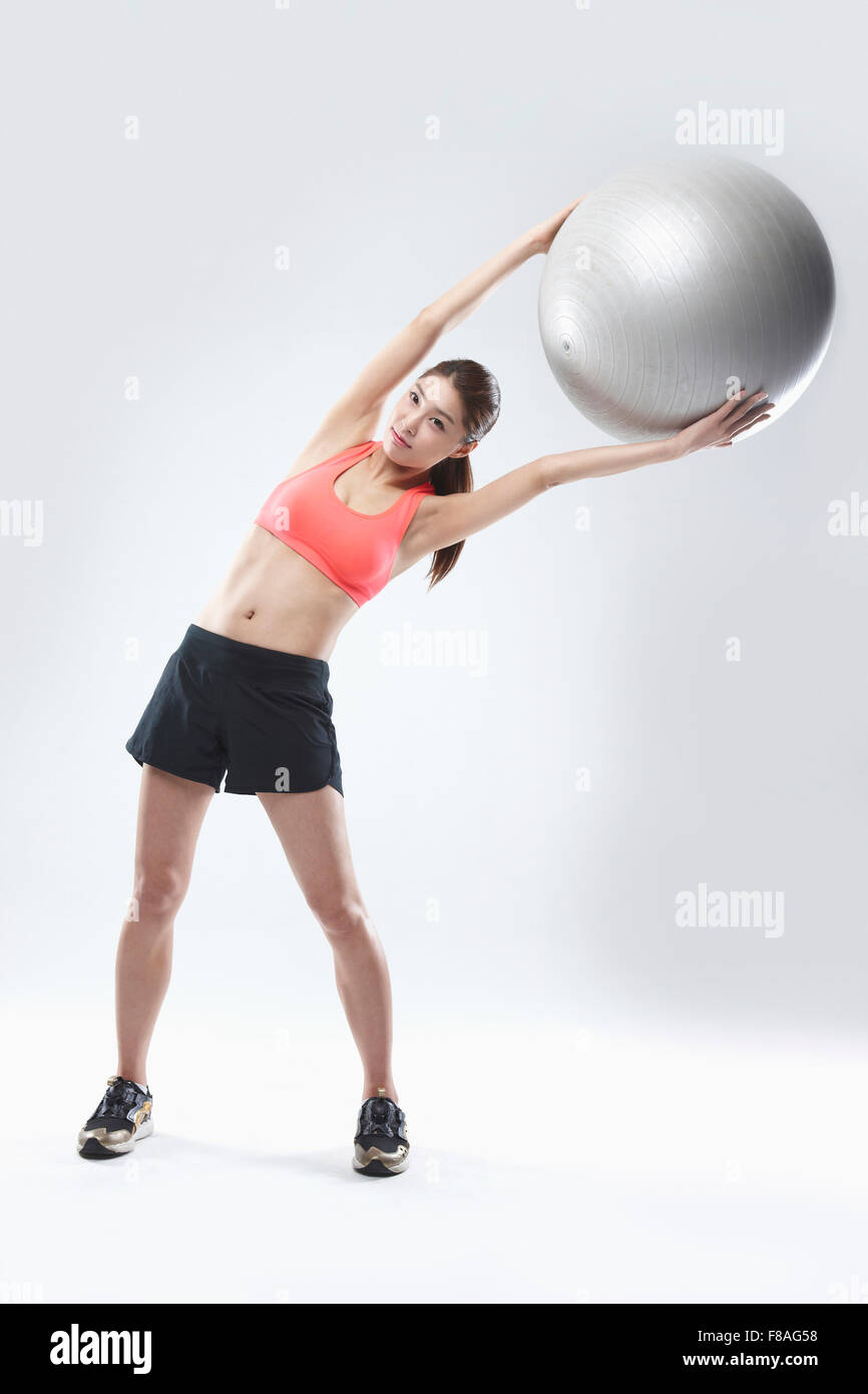 Woman in sports wear lifting a gym ball above her head and bending her upper body to the side Stock Photo